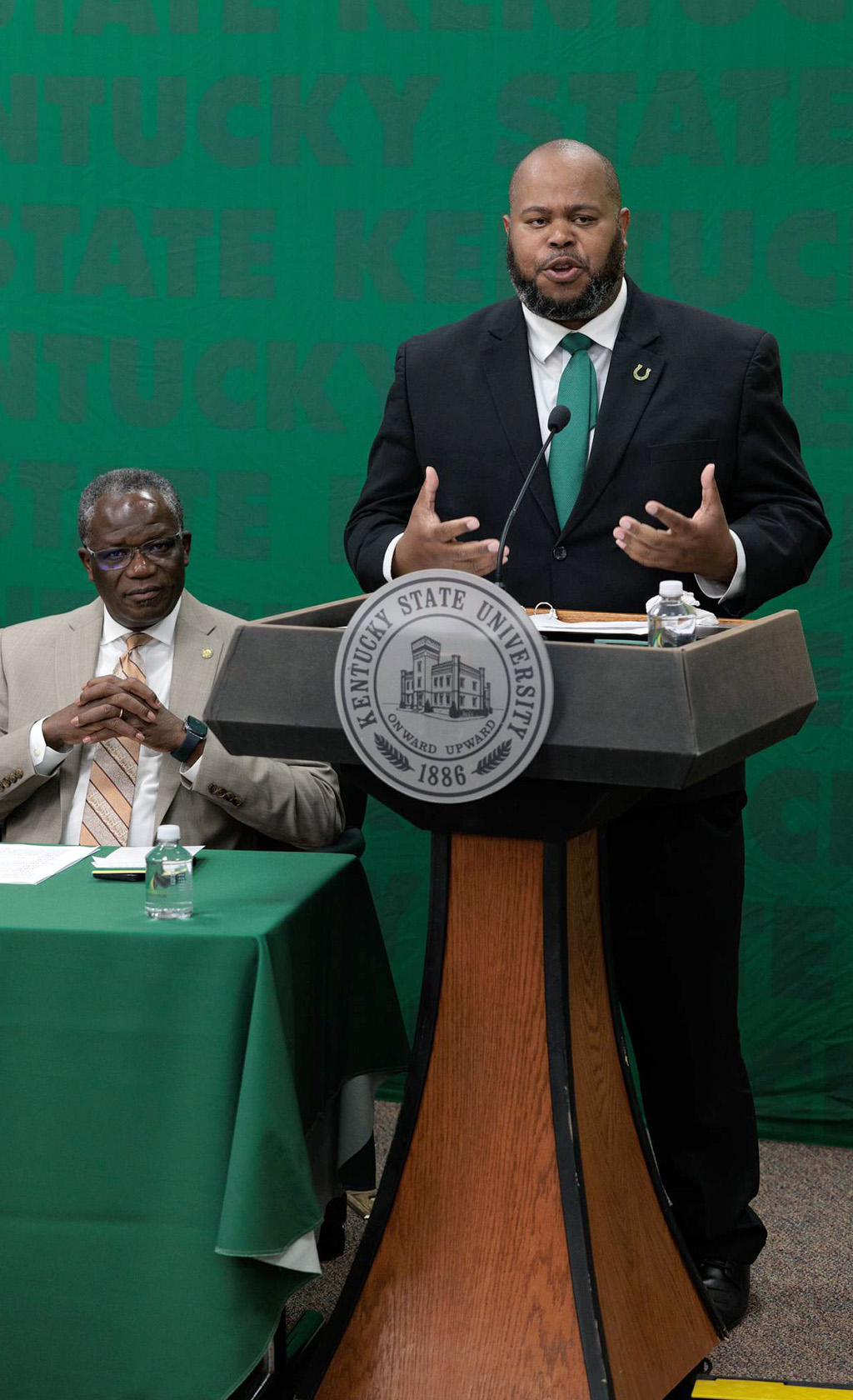 Dr. Bernard presenting at the podium with President Akakpo seated nearby
