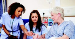 Nurses in blue scrubs checking on patient's hand